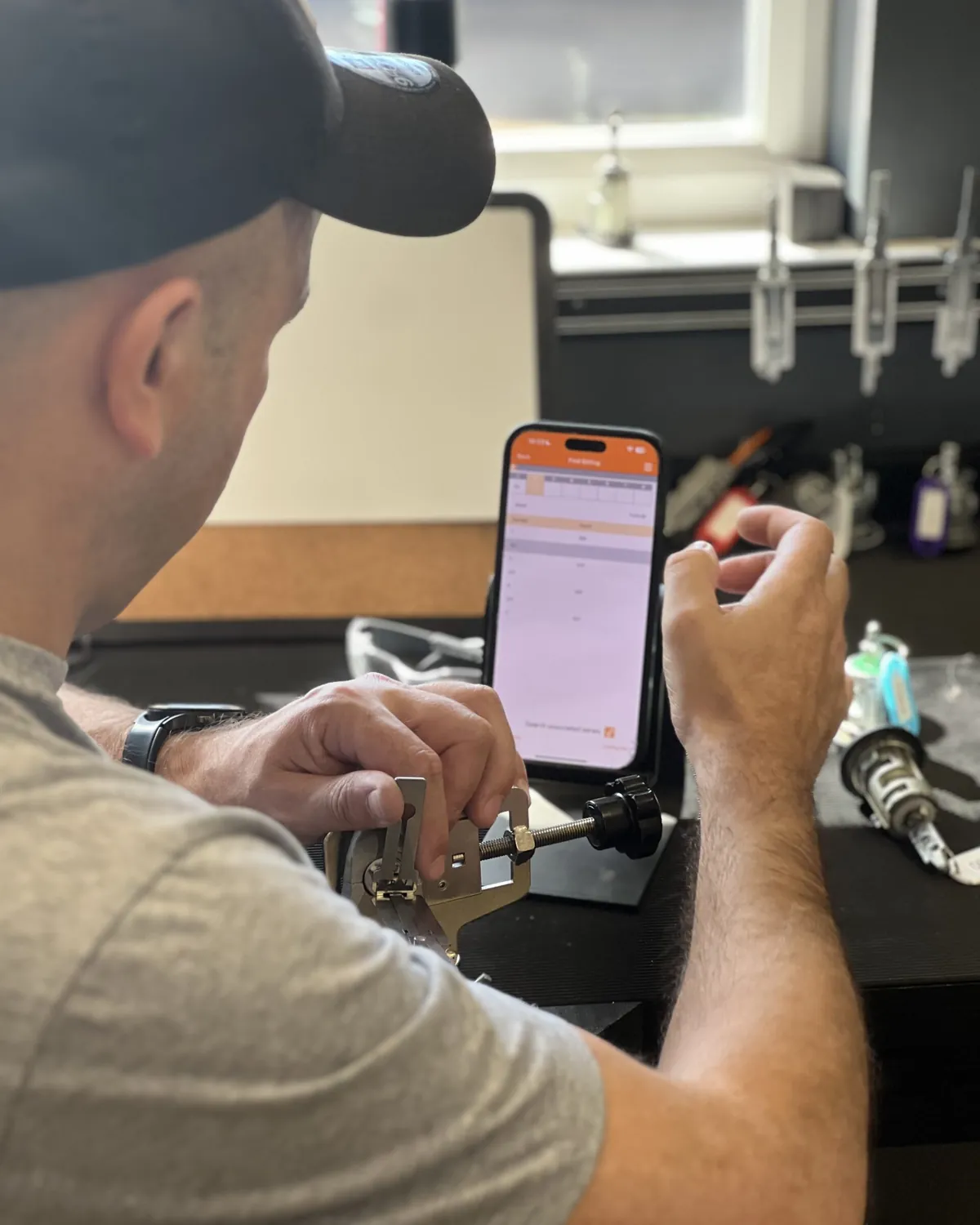 A trainee works a lock with a pick tool, the Alter Academy App open on a phone beside him