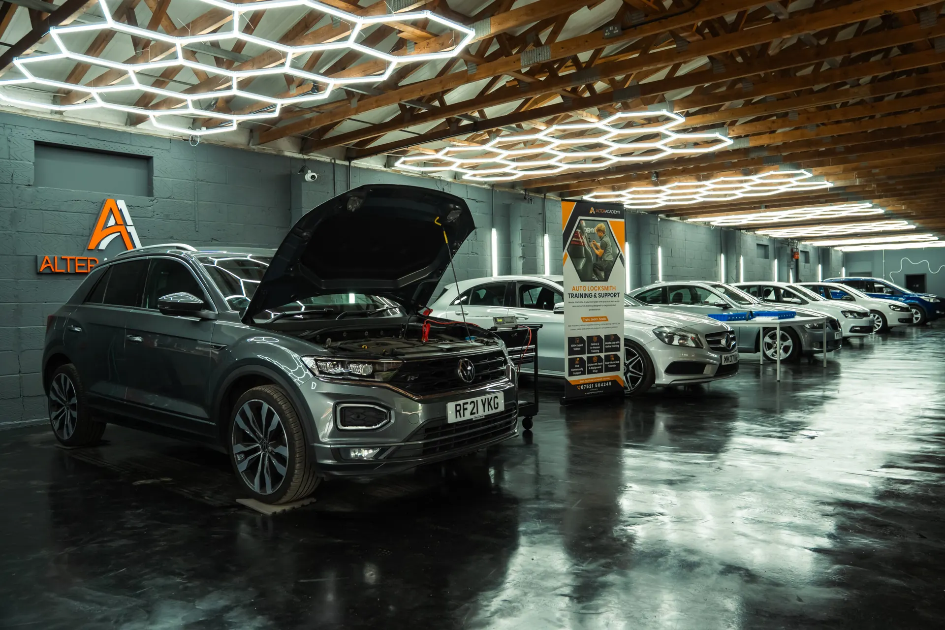 The Alter Academy workshop under hexagon lights: a VW with its bonnet up and a line of cars ready for training