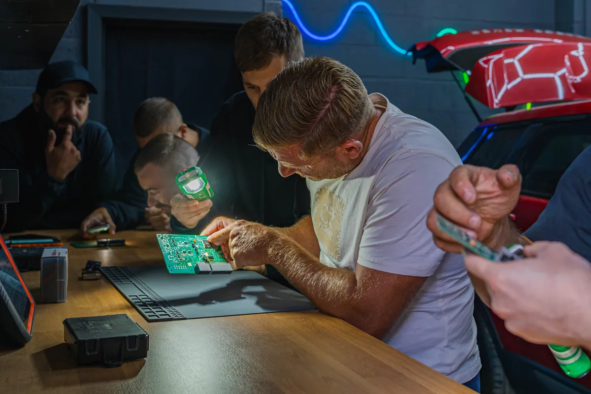 A trainer demonstrates on a circuit board while students watch closely