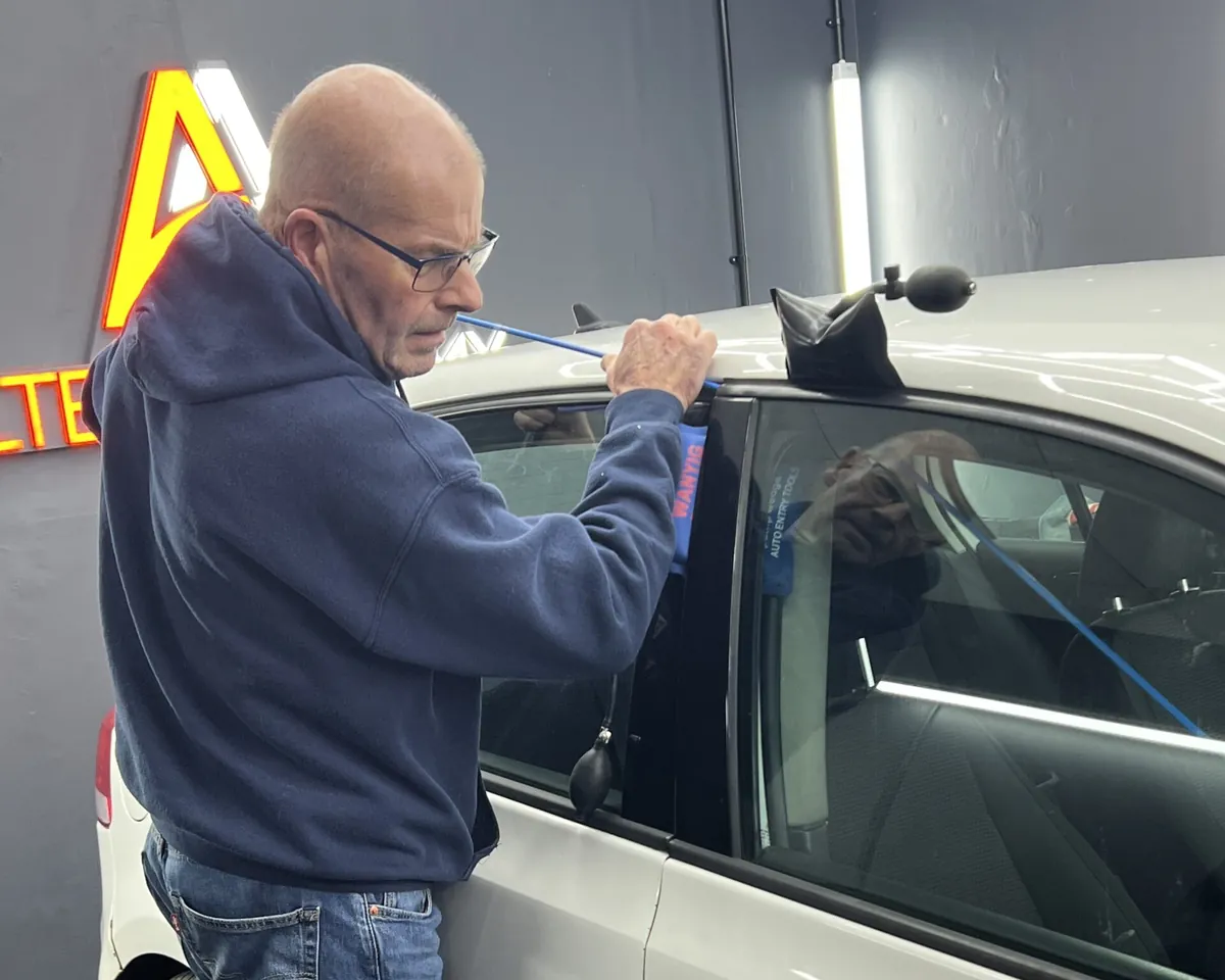 A trainee opens a car by vehicle entry with an air wedge and a long-reach tool